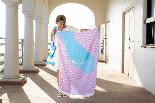 Woman holding up a LOVE from Santa Barbara Turkish towel under a seaside colonnade