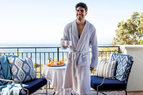 Guest in a waffle robe with breakfast on a sunny ocean-view terrace