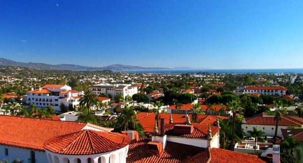 Red tile rooftops and palm trees of downtown Santa Barbara with the mountains and the Pacific Ocean under a clear blue sky