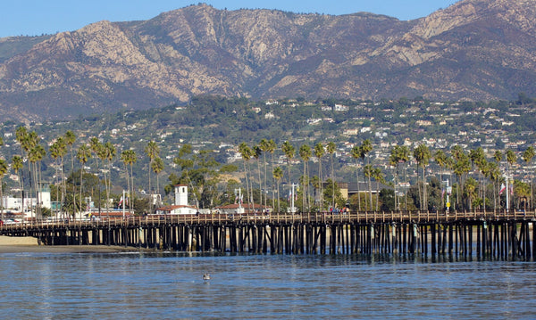 Stearns Wharf stretching across calm blue water with palm trees and the Santa Barbara foothills behind