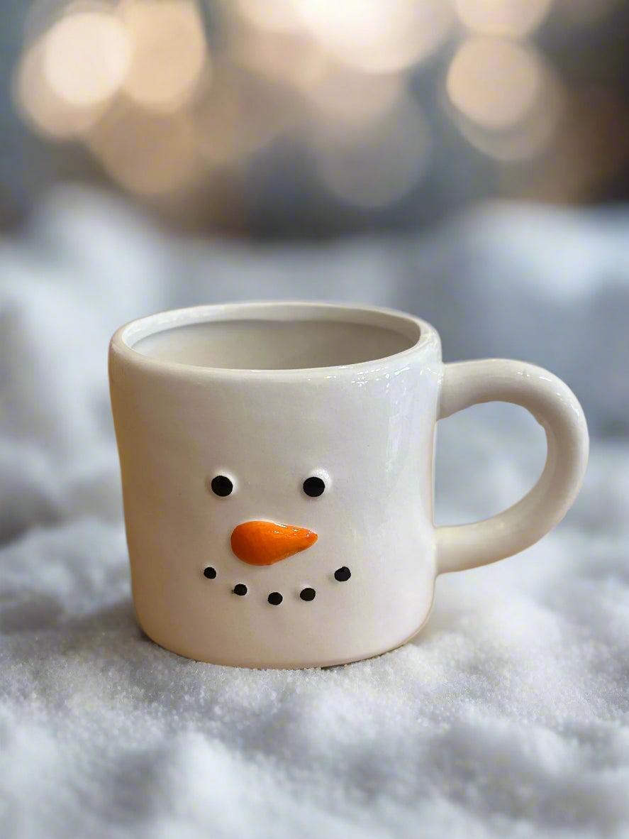 Snowman-themed mug with a carrot nose on a snowy background