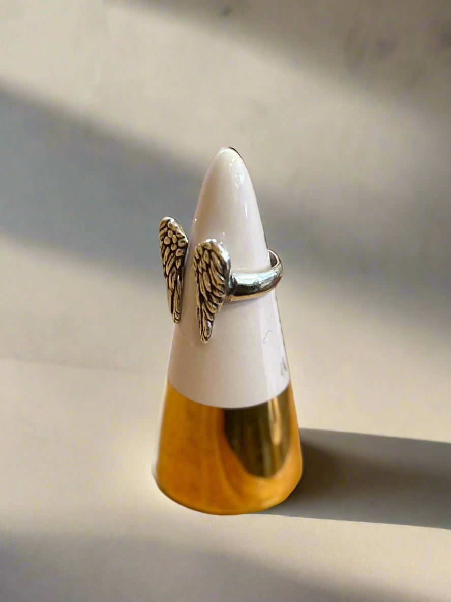 Silver ring with angel wings on a white cone-shaped stand against a blurred background