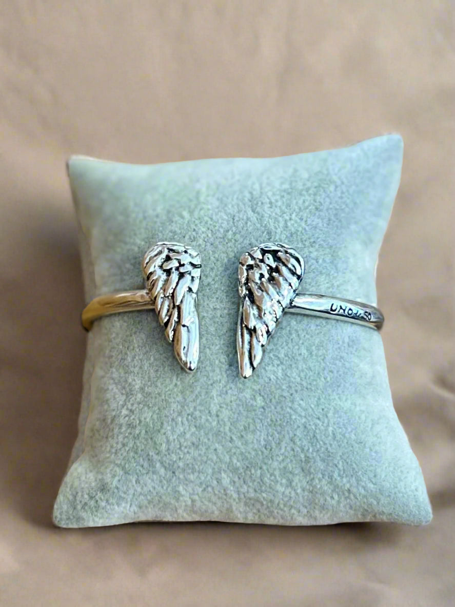 Silver angel wing rings on a light blue cushion with a wooden background