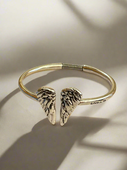 Silver bracelet with angel wing designs on a white surface