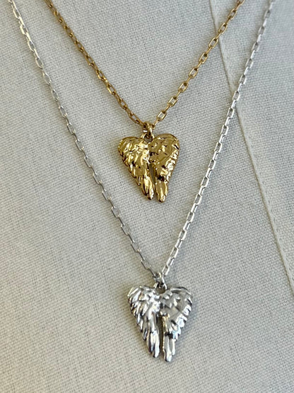 Two angel wing pendants on gold and silver necklaces against a light background