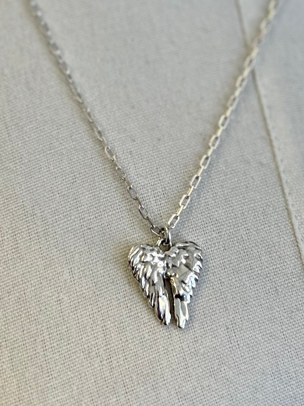 Silver heart-shaped pendant with wings on a chain against a light gray background