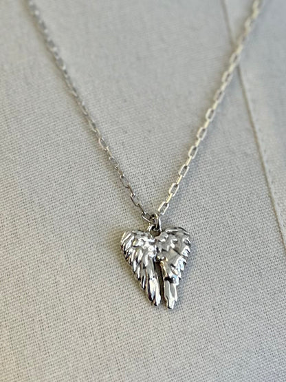 Silver heart-shaped pendant with wings on a chain against a light gray background