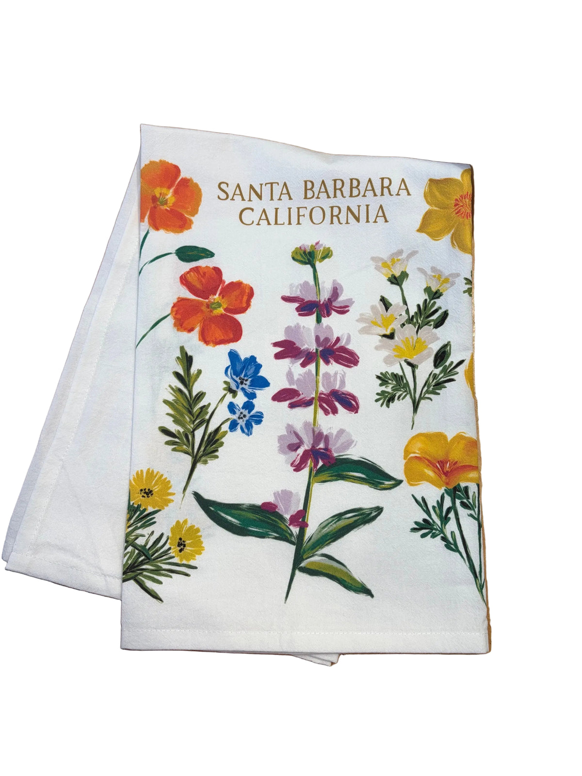 A white fabric tea towel featuring a colorful botanical illustration of wildflowers and the text 'SANTA BARBARA CALIFORNIA' printed in brown at the top, resting on a wooden table.